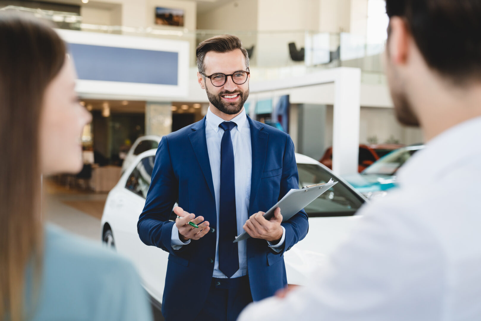 A white salesman showcasing a car to a couple at a business development car dealership.